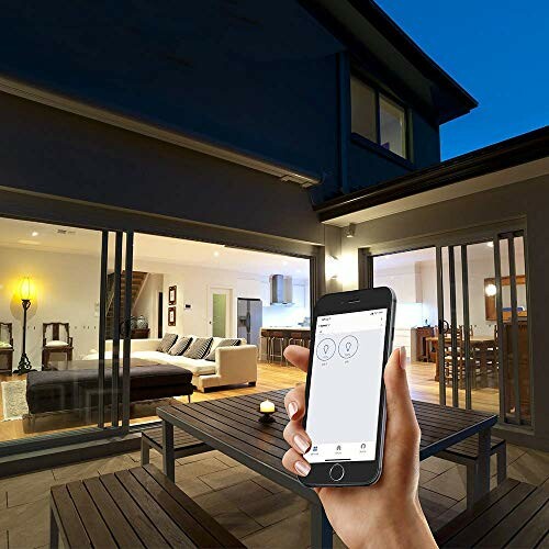 Hand holding smartphone with home automation app, modern house in background at night.